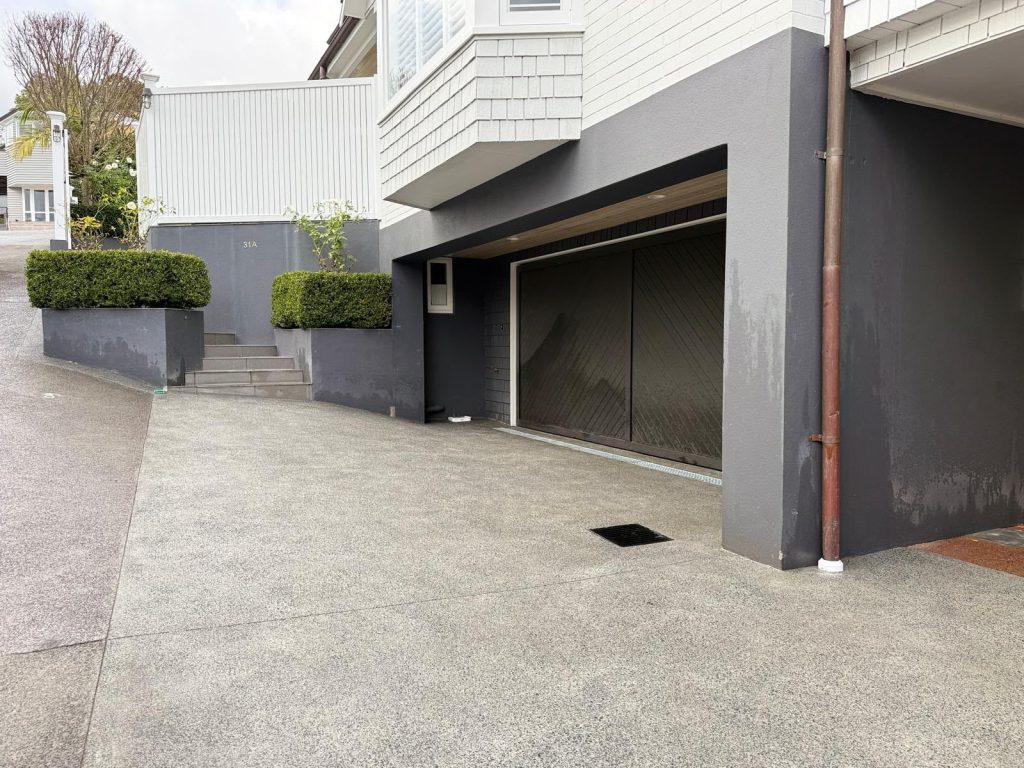 Finished concrete driveway with a new drainage grate outside a modern home
