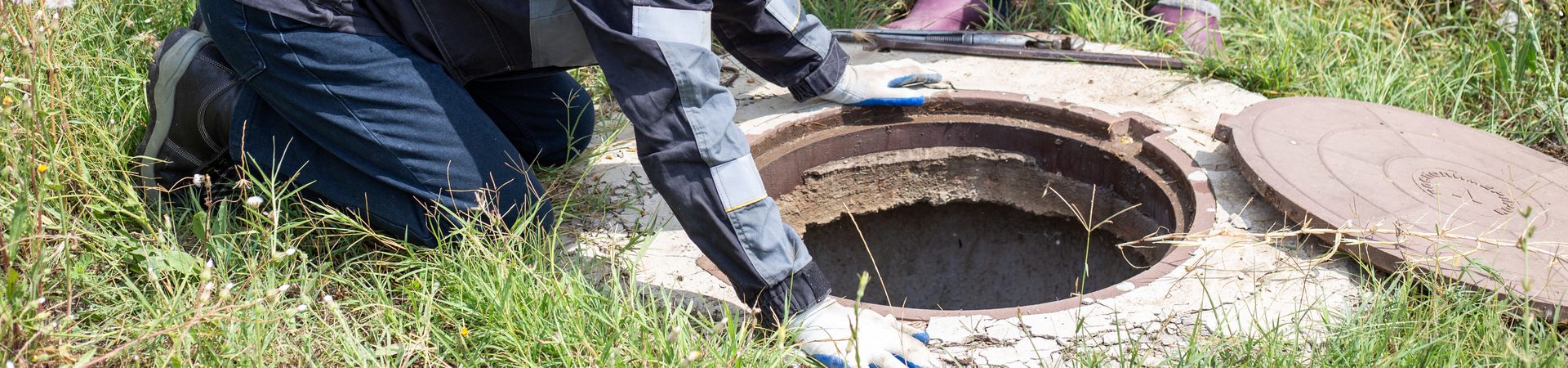 Drainlayer opening a manhole cover in long grass