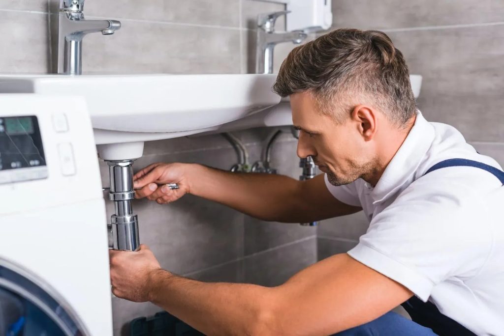 Plumber unblocking the drain trap under a bathroom basin