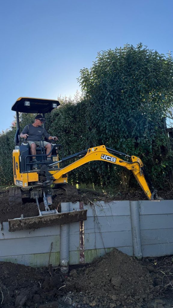 Metro Drainage drainlayer operating a JCB mini excavator beside a hedge