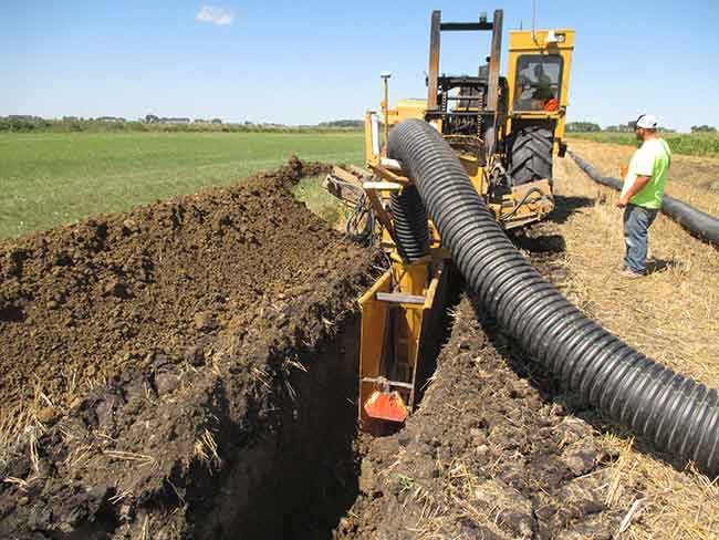 Excavator laying corrugated drainage pipe across an open field