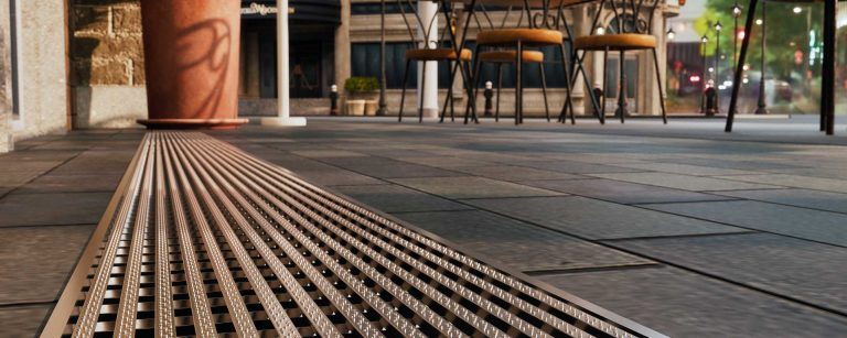 Stainless steel channel drain running along a paved public walkway